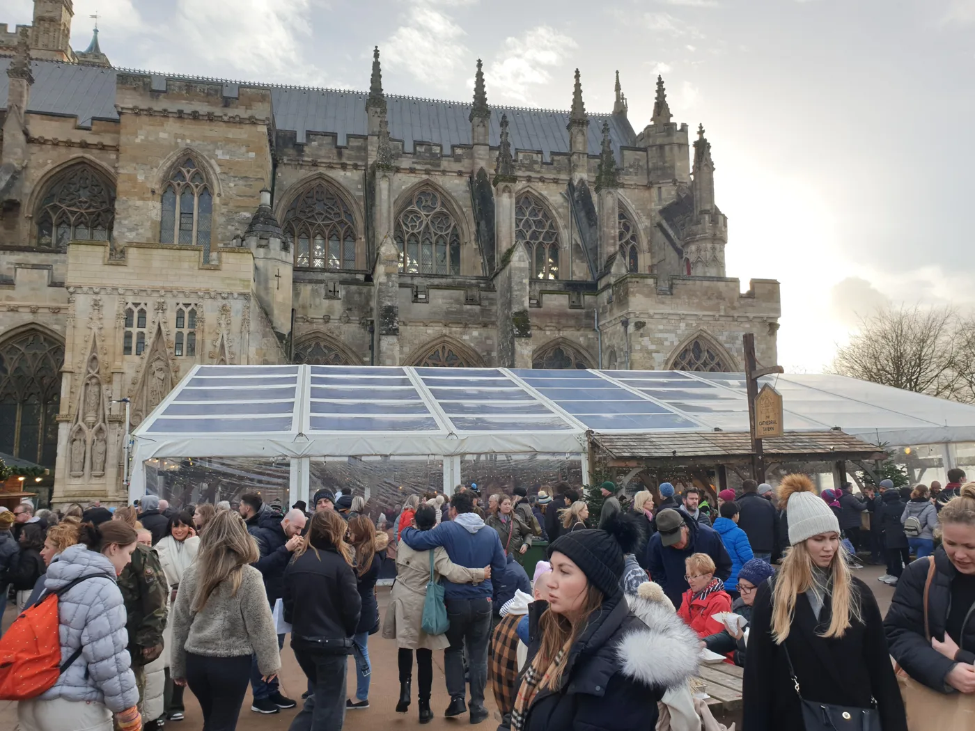 Crowds outside the Cathedral Tavern marquee at the Exeter Cathedral Christmas Market, with the cathedral behind.